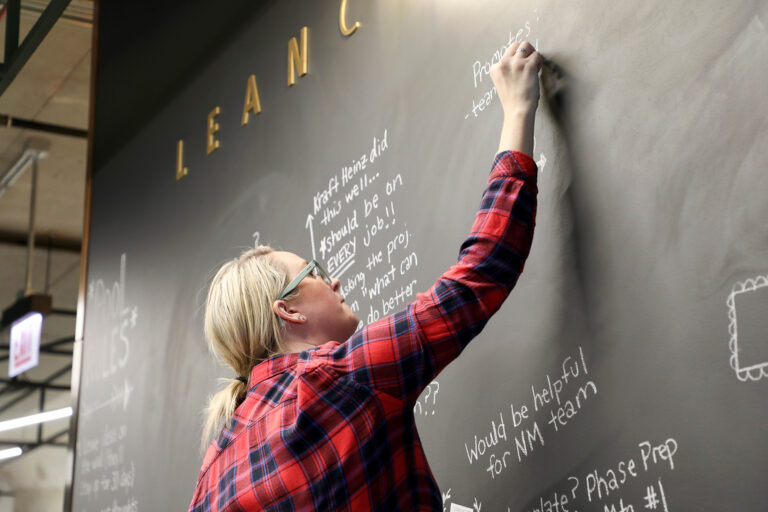 Skender team member writing notes on a large chalkboard wall in the office Lean collaboration space.