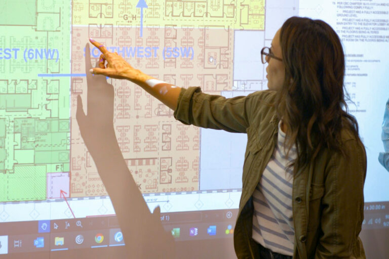 Skender team member pointing at a projected building floor plan during a planning meeting, demonstrating Lean construction process optimization.