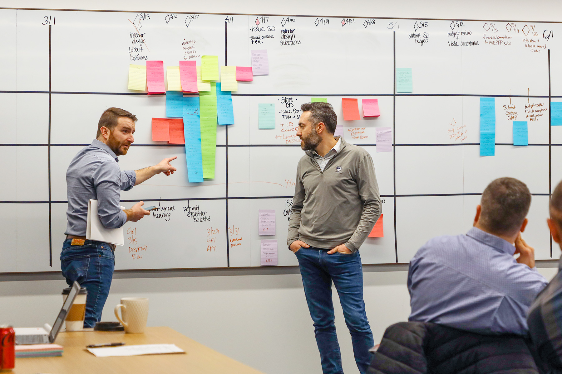 Two Skender team members reviewing a planning board covered with colorful sticky notes, discussing construction process improvements as part of their Lean approach.